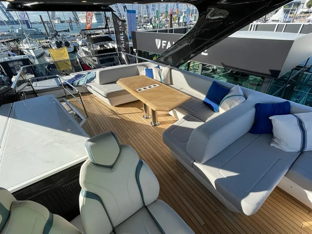 Luxurious yacht interior featuring a wooden table, grey seating, blue cushions, and a panoramic view of the marina.